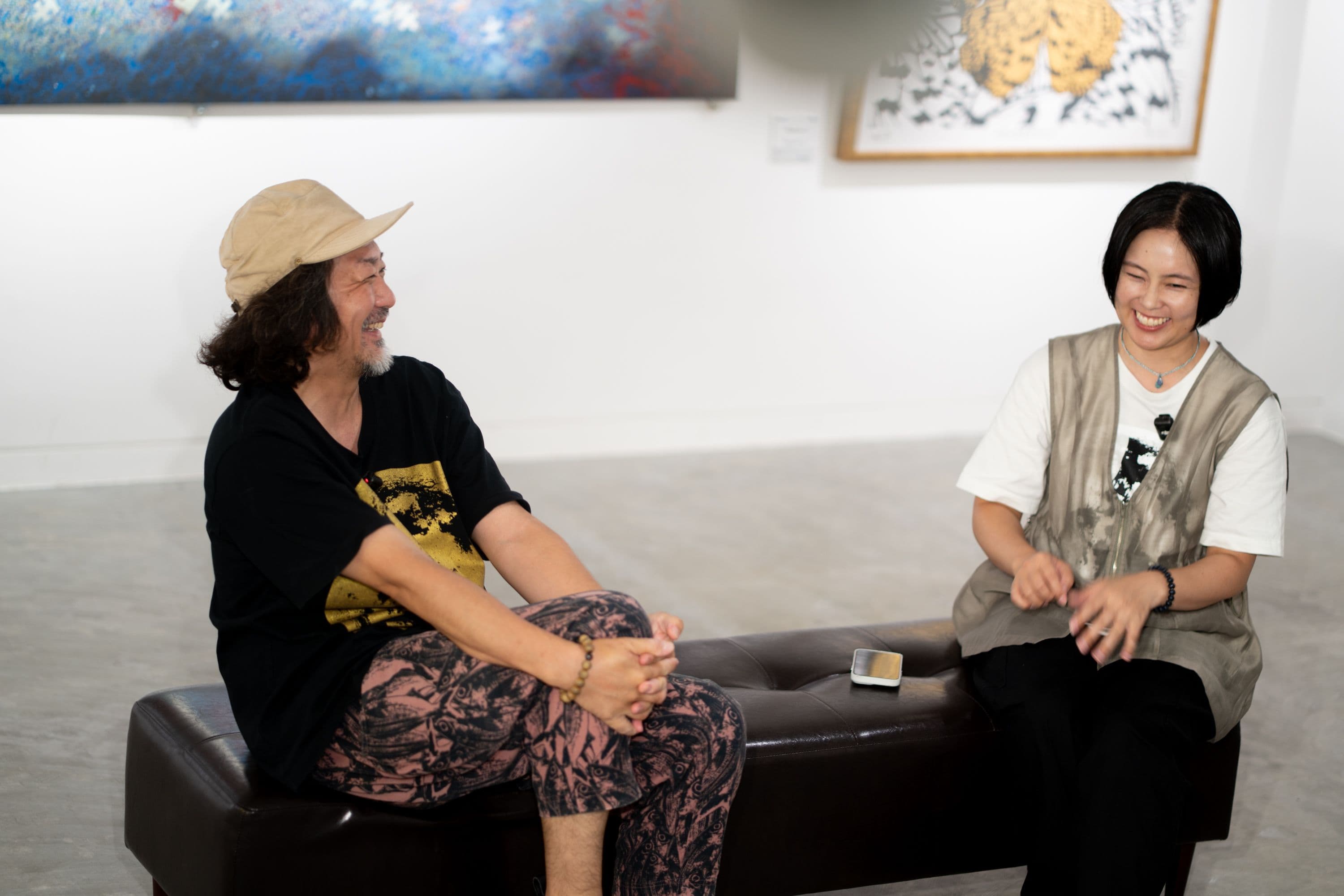 ギャラリーのベンチで笑い合う池城安武さんと村上あす美さん