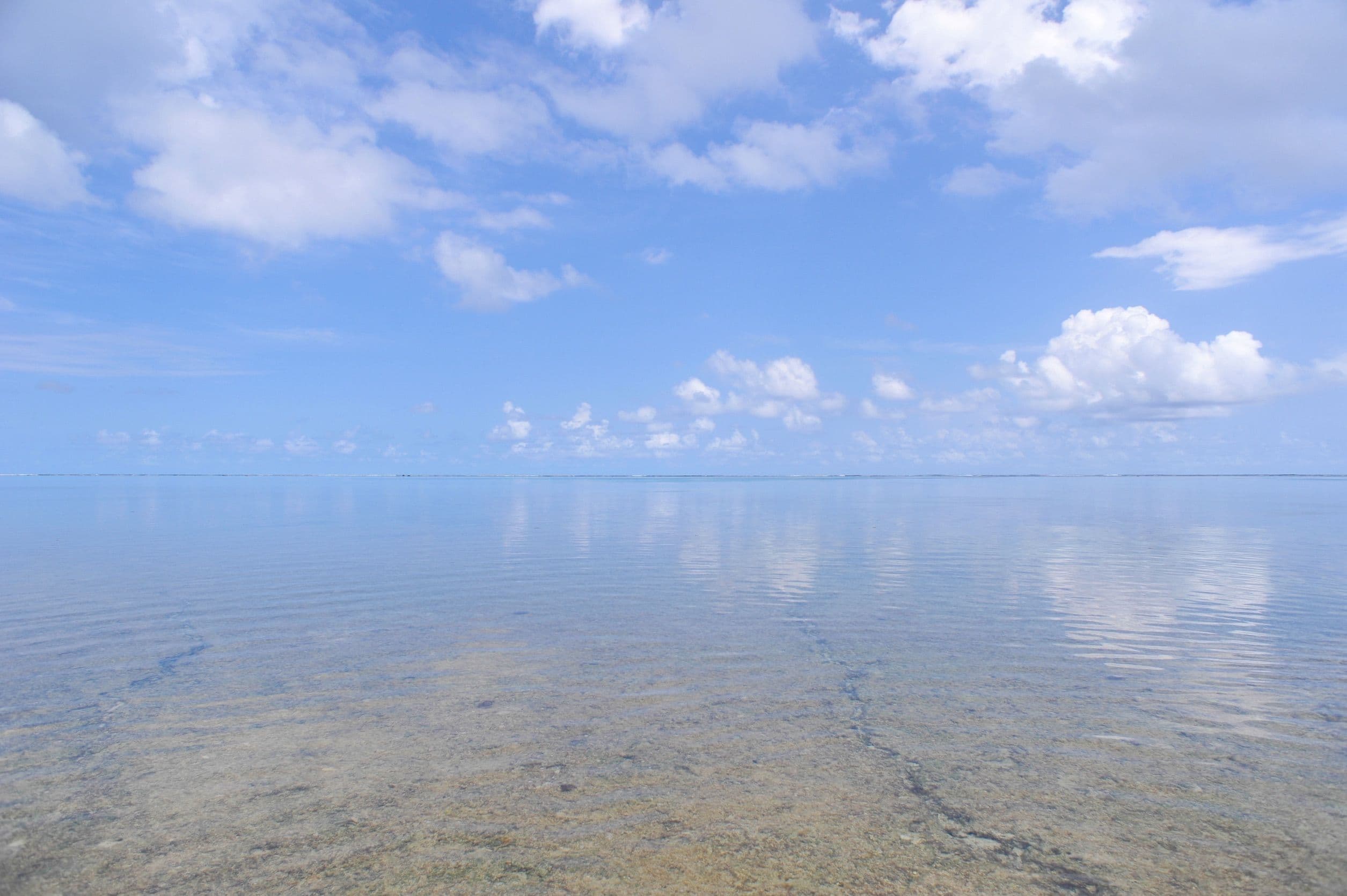 遠浅の海に青空と雲が映り込む、穏やかな海辺の風景