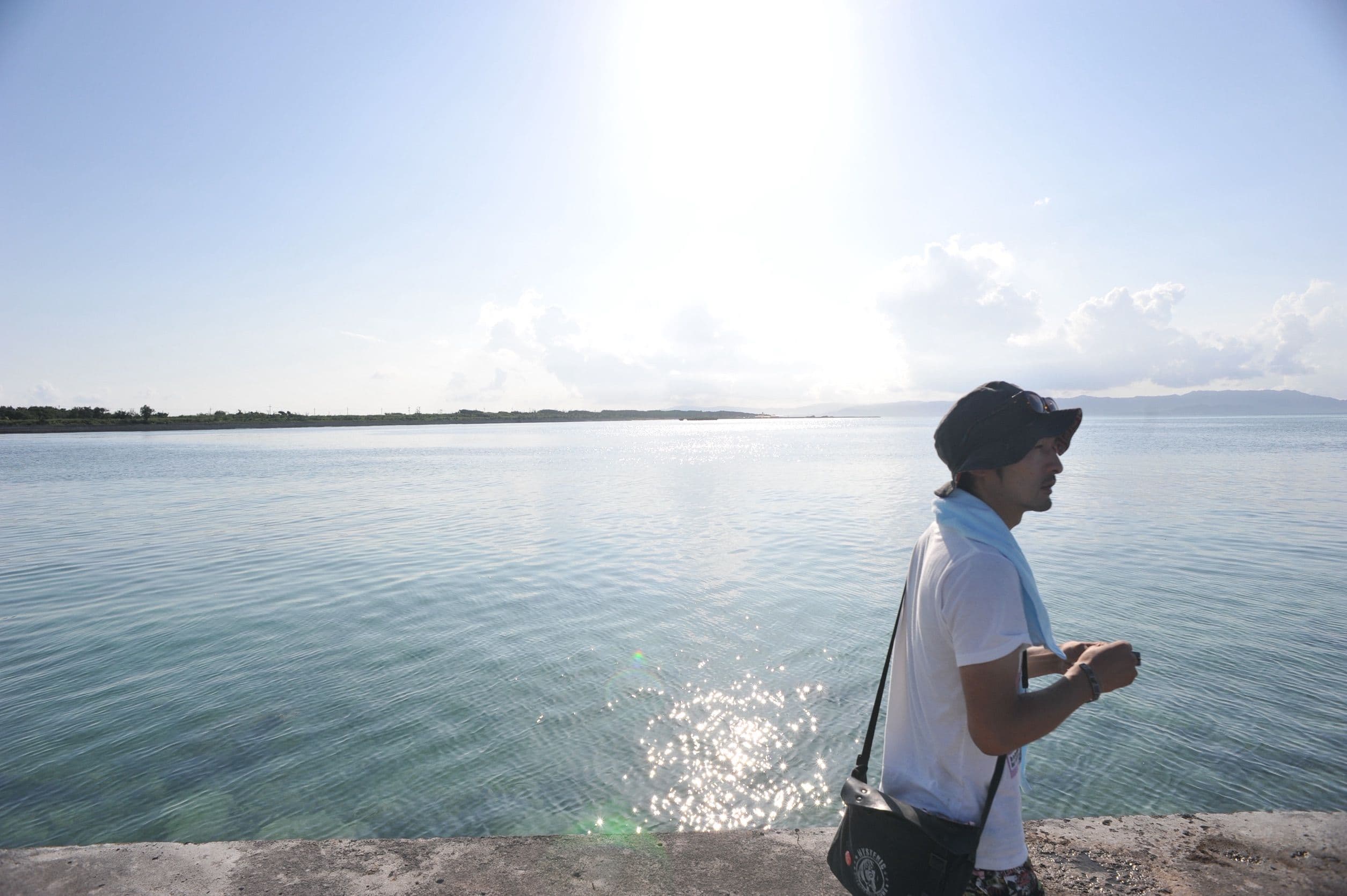 光を受けて輝く海沿いの護岸を歩く、肩掛けバッグの人物